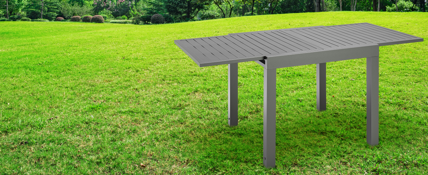 en métal gris avec surface supérieure perforée, positionnée sur une pelouse verte. Dispose d'un design rectangulaire allongé avec des pieds robustes.