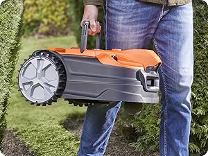 Tondeuse à gazon robotisée orange et grise utilisée à l'extérieur sur de l'herbe, avec uniquement l'appareil et les jambes du conducteur visibles.