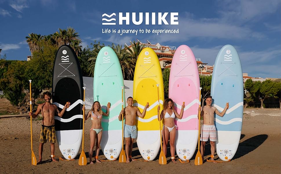 Cinq planches de surf HUIIKE de différentes couleurs (noir, vert menthe, jaune, rose et bleu clair) exposées sur une plage avec des palmiers