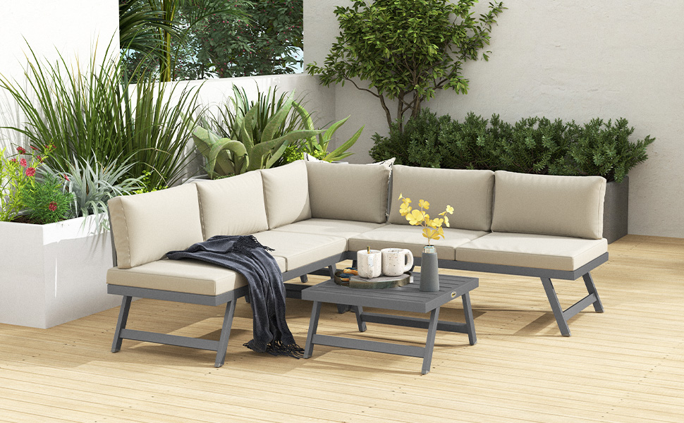avec canapé gris en L, table basse et coussins crème. Entouré de plantes en pot dans un jardin moderne et minimaliste.