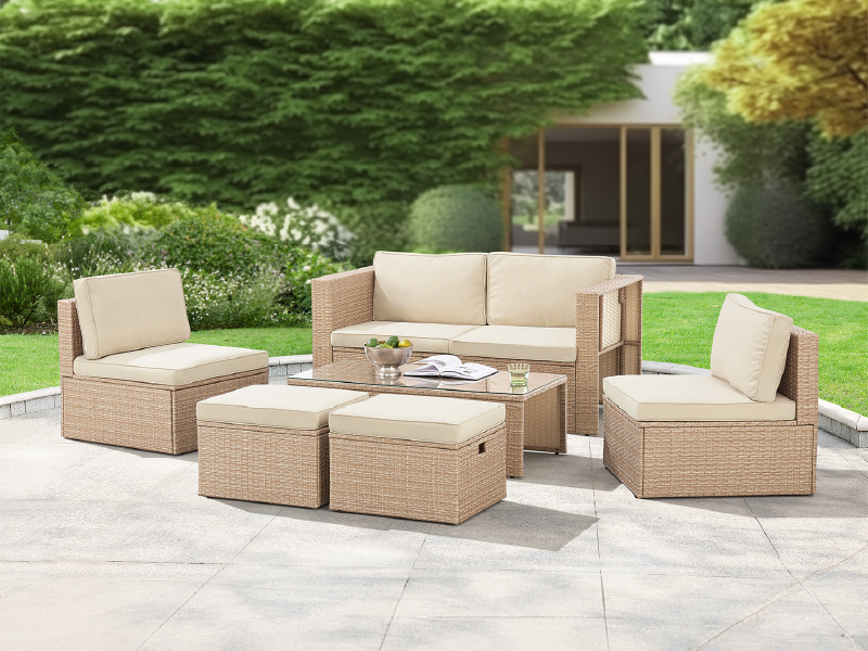 comprenant un canapé tressé beige, des chaises et une table basse disposés sur un patio en pierre avec un fond de jardin.
