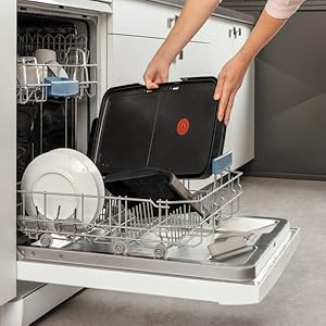 Les mains placent un récipient rectangulaire noir dans le lave-vaisselle rempli d'assiettes et de vaisselle.