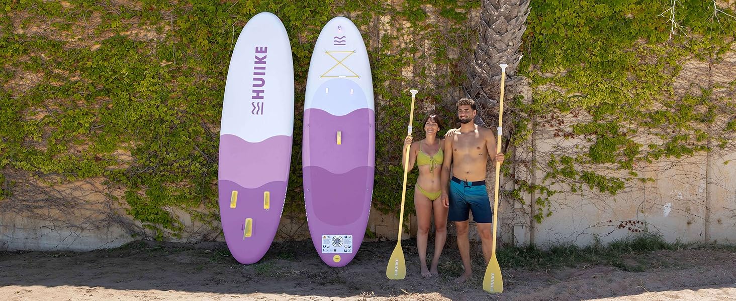 Deux planches à pagaie violettes et blanches appuyées contre une paroi rocheuse près de l'eau, avec deux personnes debout à côté d'elles.