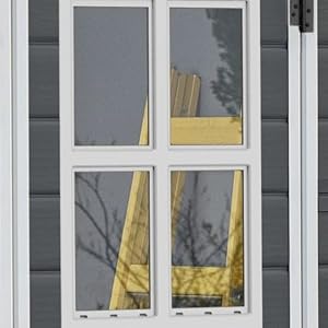 Fenêtre à cadre blanc à quatre vitres sur un revêtement gris, montrant un rideau ou un tissu jaune visible à travers les panneaux de verre.