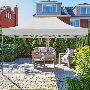 Grand auvent extérieur carré beige offrant de l'ombre sur un coin salon de patio meublé, adossé à des maisons en briques et à un aménagement paysager de jardin.