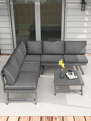 avec canapé sectionnel gris en L et table basse assortie sur une terrasse en bois. Le revêtement blanc et les portes vitrées sont visibles à l'arrière-plan.