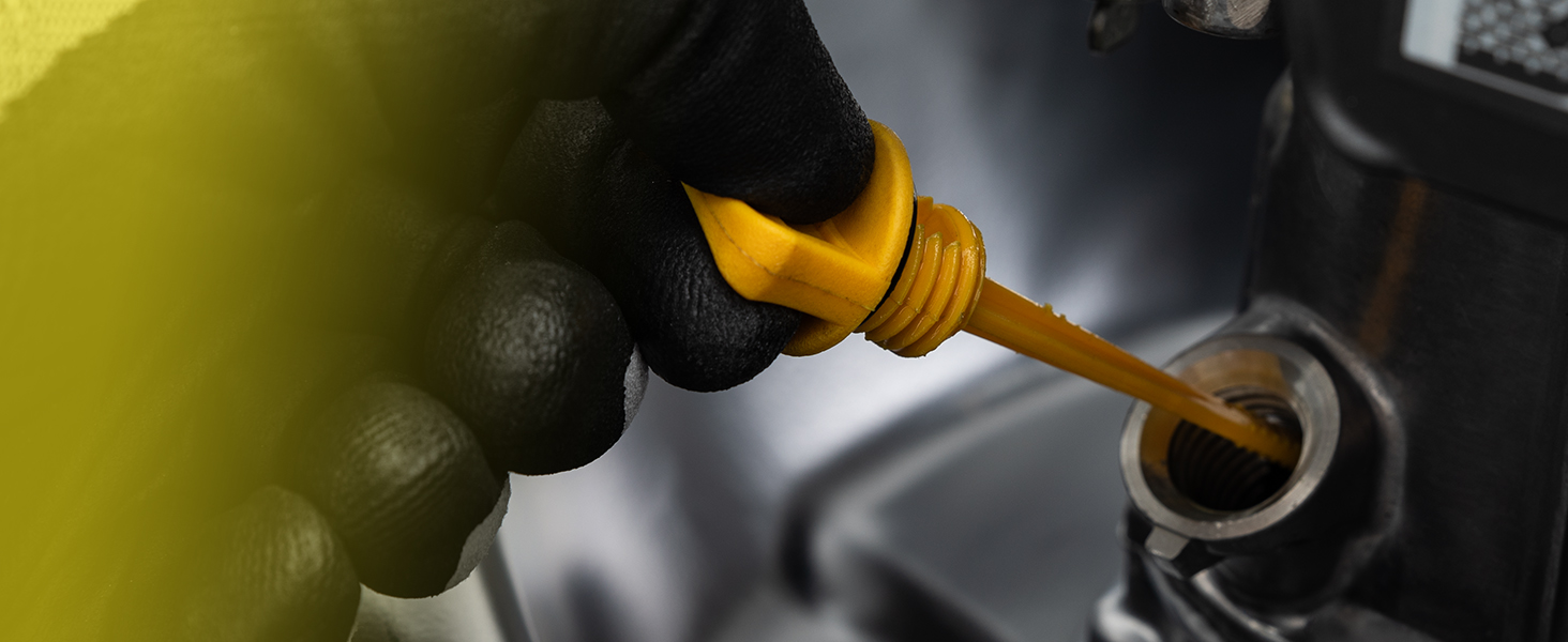 Gros plan d'une main dans un gant noir versant de l'huile à moteur jaune dans un moteur de voiture à partir d'un récipient à long col