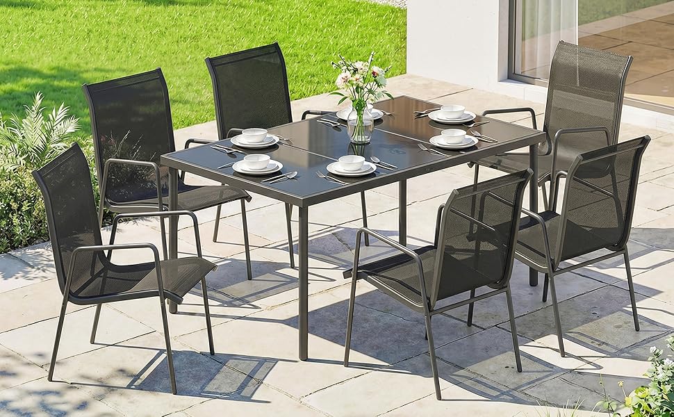 Ensemble de meubles de patio d'extérieur comprenant une table à manger à cadre en métal noir avec plateau en verre et six chaises en maille noire assorties disposées dans un jardin avec un tapis d'extérieur bleu.