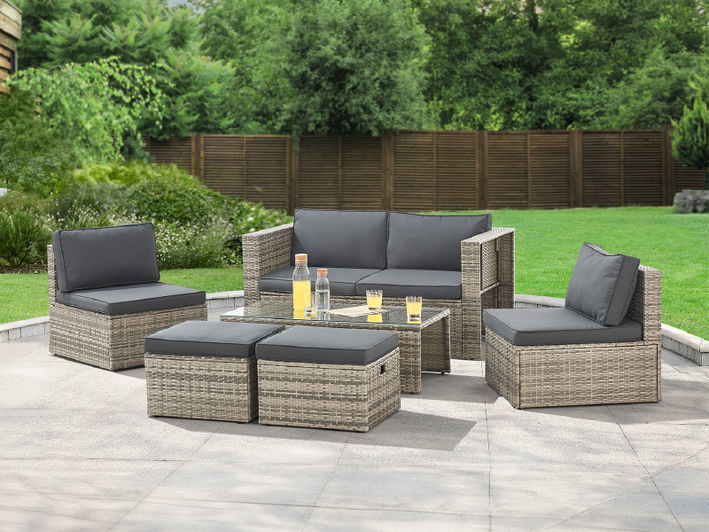 avec des meubles en osier tressé comprenant une causeuse, deux chaises et deux poufs. Des coussins gris et une table avec plateau en verre complètent l'ensemble