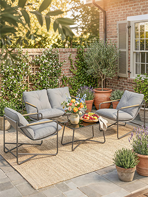 Ensemble de conversation en plein air en trois pièces avec des chaises rembourrées grises et une petite table d'appoint ronde sur un patio en pierre, entouré de plantes en pot et d'un bâtiment en brique.