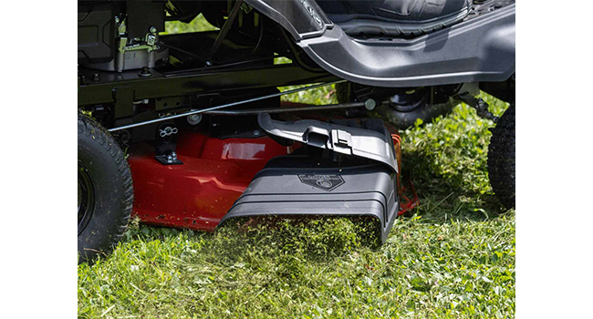 Tondeuse à gazon en action sur l'herbe, montrant une vue partielle du corps de tondeuse rouge et gris pendant l'utilisation à l'extérieur.