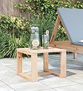 Table d'extérieur en bois sur terrasse carrelée avec fond de jardin, plantes en pot et chaise longue bleue visible dans un cadre paysager.