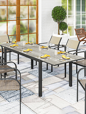 Ensemble de salle à manger d'extérieur comprenant une table et des chaises en métal gris avec un motif décoratif, illustré sur le patio avec des plantes topiaires en pot sous plusieurs angles.