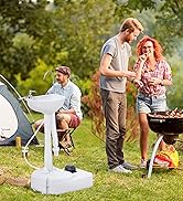 Une famille de quatre personnes s'est réunie autour d'un barbecue extérieur et d'une installation de camping dans une cour verdoyante et arborée. Homme en train de griller, femme et enfants à proximité, tente et mobilier d'extérieur blanc visibles.