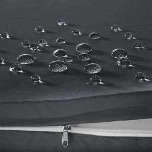 Gros plan de gouttelettes d'eau sur une surface foncée et texturée. Une fermeture éclair est visible le long du bord, ce qui suggère un tissu imperméable ou résistant à l'eau