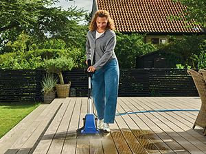 Séquence du nettoyage d'une terrasse extérieure, montrant une personne utilisant de l'équipement de nettoyage sur la surface d'une terrasse en bois dans la cour arrière.