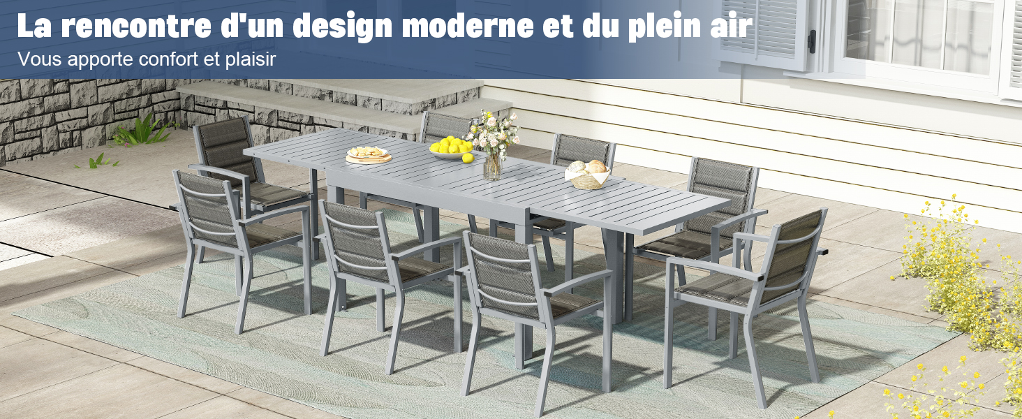 avec table rectangulaire grise et huit chaises assorties sur un patio en pierre. Le bâtiment aux parois blanches en arrière-plan suggère un cadre résidentiel