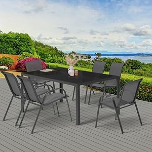 avec table foncée et six chaises sur une terrasse en bois. Fond pittoresque avec vue sur l'eau, arbres et plantes à fleurs.
