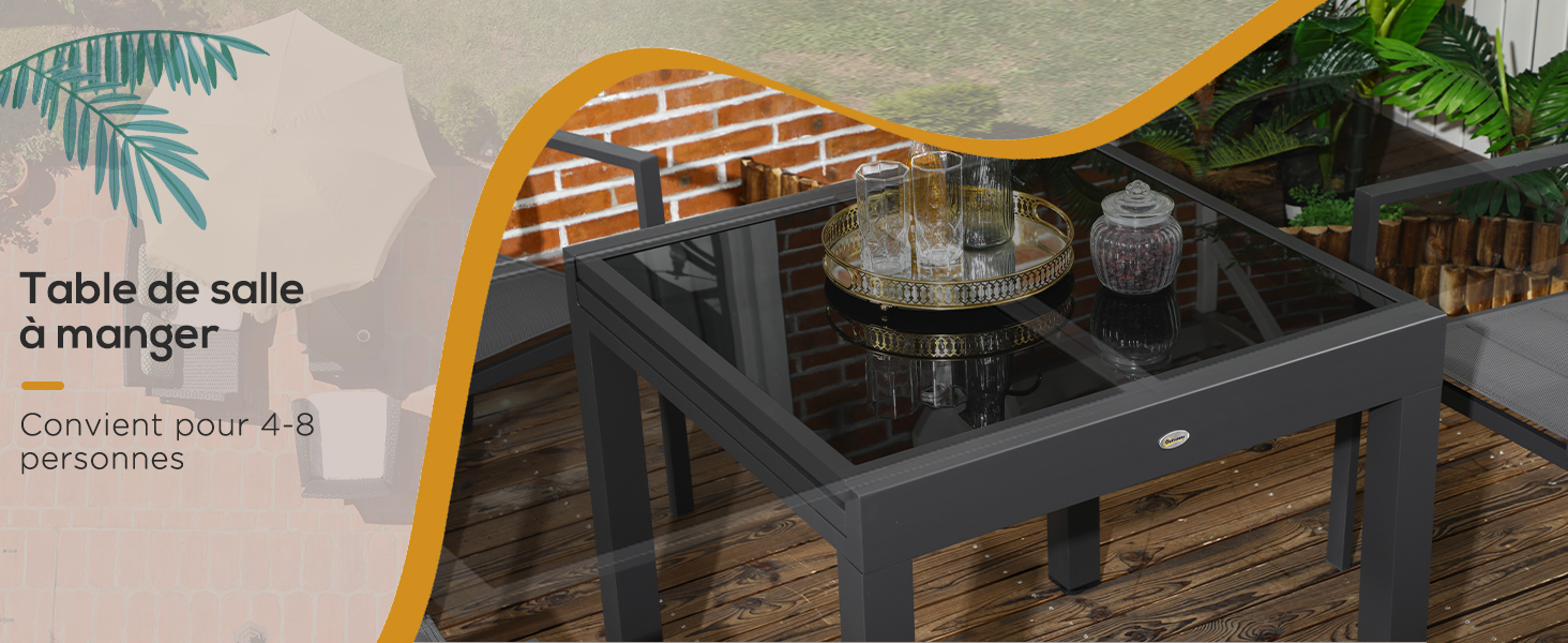 avec table en verre et quatre chaises. Cadre sombre, adapté pour 4 à 6 personnes, situé sur une terrasse en bois avec fond de feuillage.
