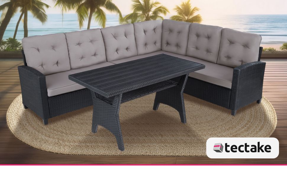 avec table basse. Coussins gris sur structure en osier foncé. Situé sur une terrasse en bois surplombant la plage et les palmiers.