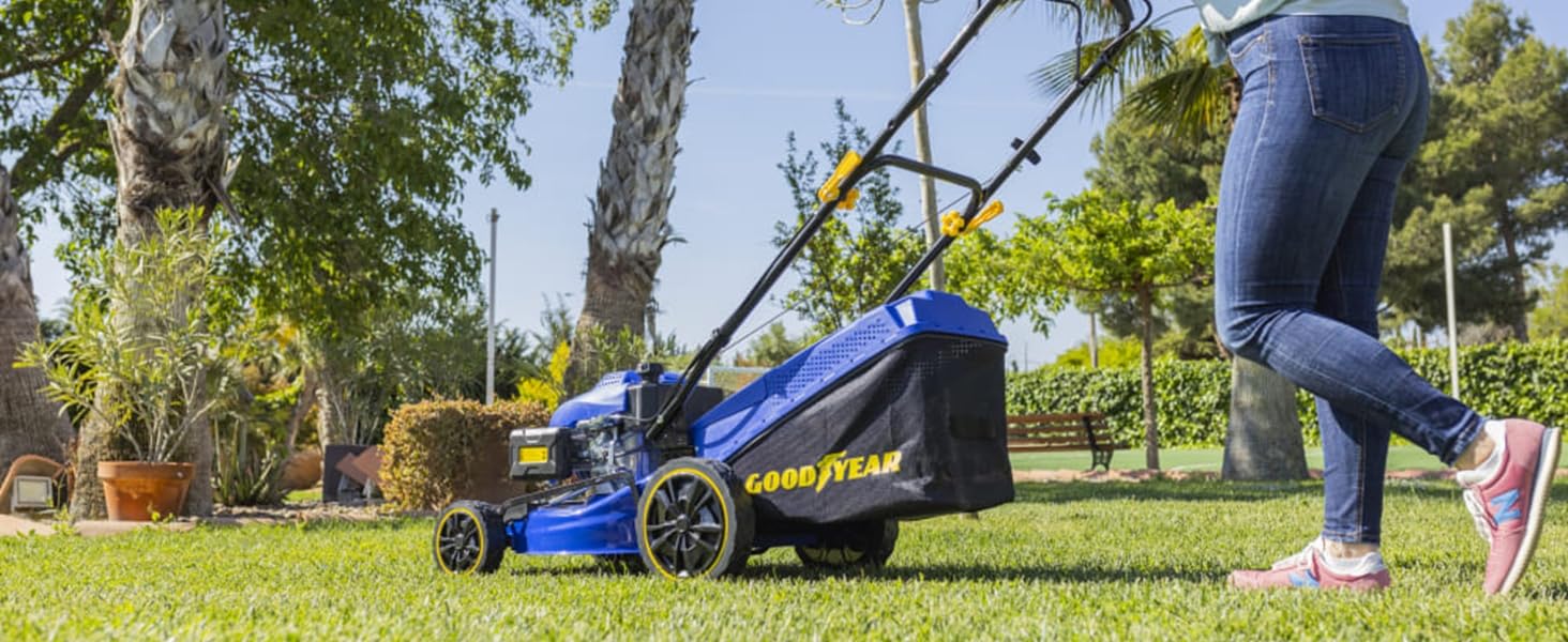 Tondeuse à gazon électrique bleue utilisée sur une pelouse verte, avec vue partielle de l'opérateur en jean poussant la machine dans un jardin ensoleillé.