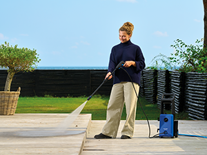 Scène extérieure avec une personne utilisant un nettoyeur haute pression bleu ou un équipement de nettoyage sur une surface en béton.