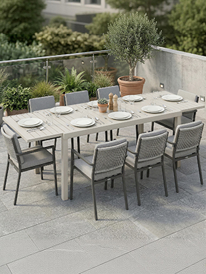 Ensemble de salle à manger pour terrasse extérieure comprenant une grande table rectangulaire avec des chaises grises, contre un mur de jardin avec des plantes en pot.
