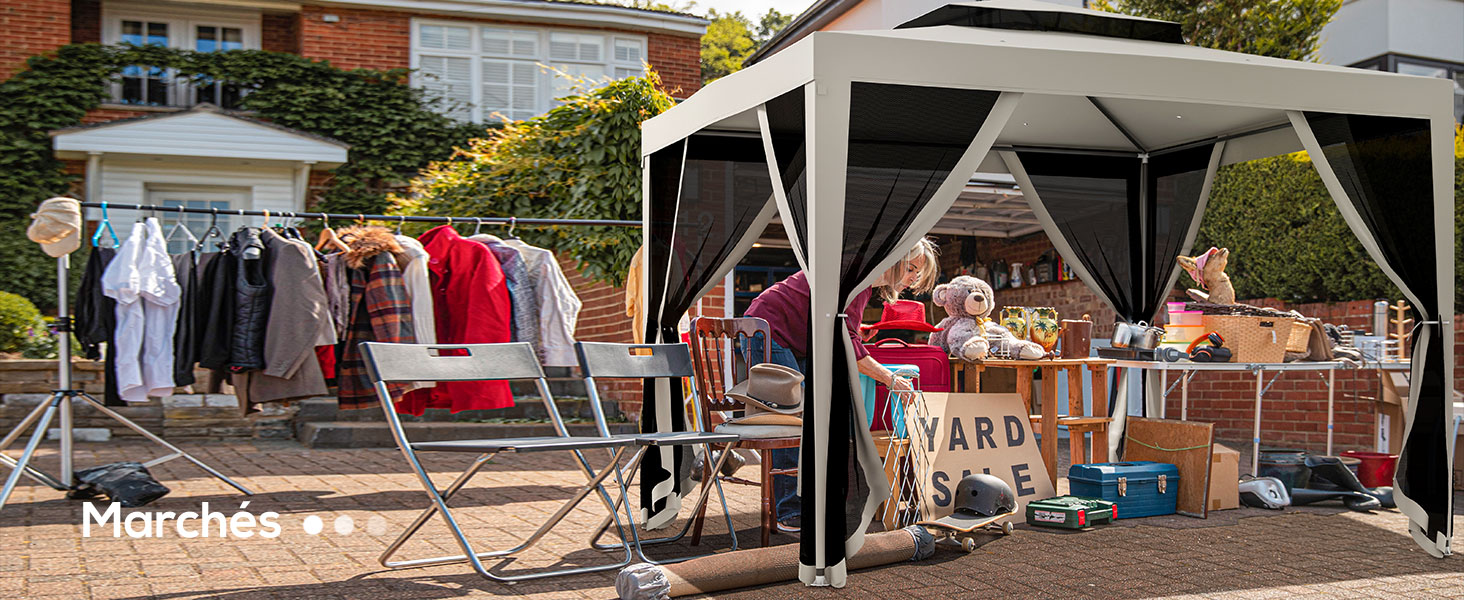 Installation de vide-grenier en plein air avec un porte-vêtements présentant divers vêtements et une tente à baldaquin escamotable blanche abritant des tables avec des marchandises variées.