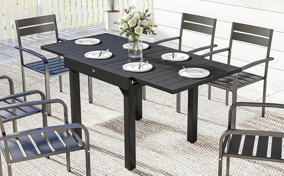 Ensemble de salle à manger d'extérieur comprenant une table extensible en métal noir avec plusieurs couverts et des chaises assorties. La table est sertie d'assiettes blanches et décorée d'un centre de table floral.