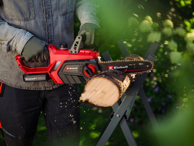 Le texte se lit comme suit : « Image 4 ». Tronçonneuse électrique rouge en cours d'utilisation, coupant du bois sur un support de sciage. L'opérateur porte des gants de protection visibles.