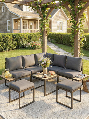 Ensemble de meubles de patio extérieur avec des cadres sombres et des coussins gris, y compris des chaises et des tables d'appoint disposées sur un patio en pierre avec fond de jardin paysager.