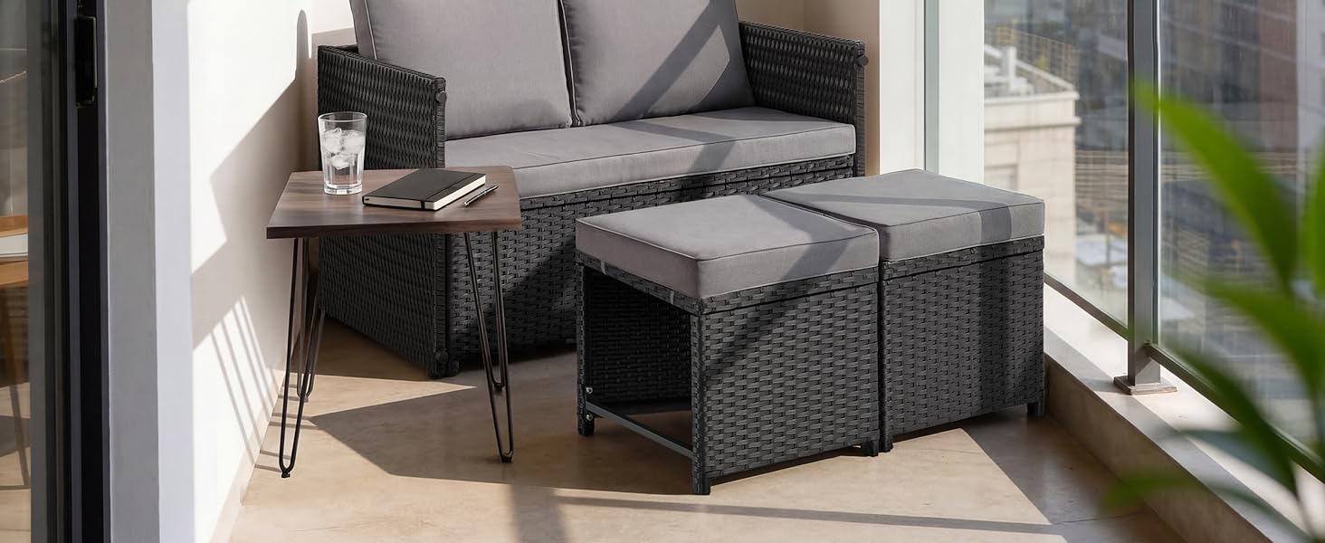 Ensemble de meubles de patio d'extérieur en rotin comprenant un canapé sectionnel tissé foncé et une table ottomane de rangement sur une terrasse moderne avec balustrade en verre et verdure.