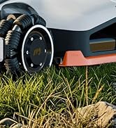 Gros plan des roues de la tondeuse à gazon robotisée et de la garniture orange contre l'herbe. Roues noires avec des bandes de roulement profondes visibles au premier plan.