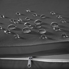 Gros plan de gouttelettes d'eau sur une surface lisse et foncée avec une fermeture éclair partiellement visible, suggérant un matériau résistant à l'eau ou imperméable