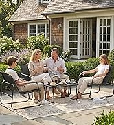 Patio résidentiel extérieur avec cinq personnes assises dans des chaises en métal gris autour d'une table en bois sur un grand tapis rectangulaire, avec jardin paysager et toile de fond de maison en brique.