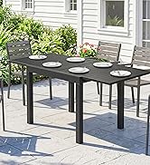 Table à manger d'extérieur rectangulaire noire avec quatre chaises grises sur le patio avec tapis décoratif bleu, extérieur de la maison blanche et feuillage vert visible.