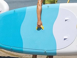 Gros plan des mains qui nettoient ou entretiennent la surface d'une planche de surf ou de paddleboard bleu clair sur fond d'eau.