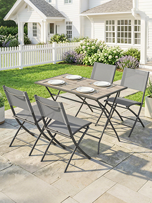 Meubles de jardin extérieurs installés sur un patio en béton avec maison blanche et clôture en arrière-plan. L'ensemble comprend des chaises pliantes et une table en métal gris et matériaux en maille.